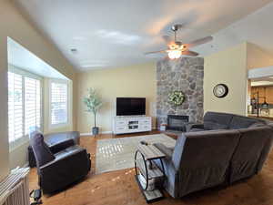 Living room with ceiling fan, a fireplace, wood finished floors, vaulted ceiling, and visible vents