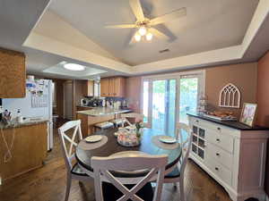Dining area featuring visible vents, lofted ceiling, ceiling fan, dark wood-style floors, and a raised ceiling