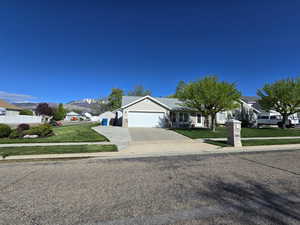 Ranch-style house with an attached garage, driveway, a mountain view, and a front lawn
