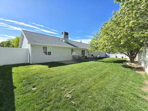 Back of house with a lawn, fence, a chimney, and roof with shingles
