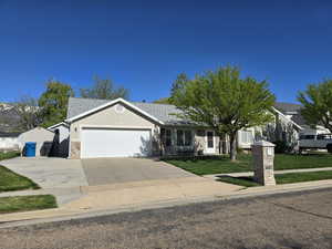 Single story home with a front lawn, stone siding, a shingled roof, concrete driveway, and an attached garage