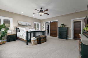 Carpeted bedroom with ceiling fan, a barn door, and a walk in closet