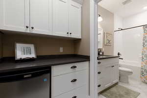 Kitchen with white cabinetry, stainless steel dishwasher, sink, and light tile patterned floors