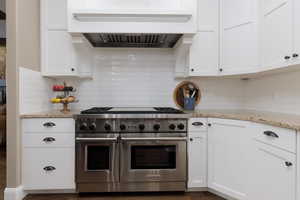 Kitchen featuring white cabinetry, custom exhaust hood, and range with two ovens