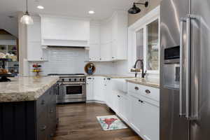Kitchen featuring high quality appliances, sink, white cabinets, hanging light fixtures, and light stone countertops