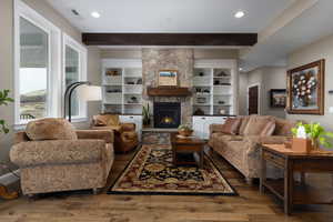 Living room featuring beam ceiling, a stone fireplace, and dark hardwood / wood-style flooring