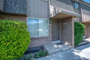 Property entrance with roof with shingles, board and batten siding, mansard roof, and brick siding