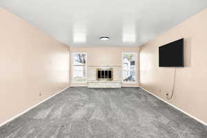 Unfurnished living room featuring baseboards, carpet flooring, a healthy amount of sunlight, and a fireplace