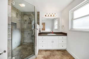 Bathroom with baseboards, tile patterned flooring, a stall shower, and vanity