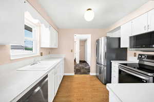 Kitchen with light countertops, white cabinets, a sink, light wood finished floors, and appliances with stainless steel finishes