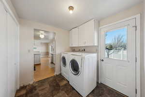 Clothes washing area featuring stone finish floor, baseboards, cabinet space, and washer and clothes dryer