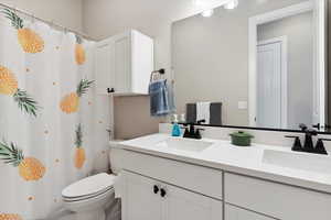 Full bath with toilet, a shower with curtain, double vanity, and a sink