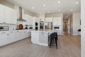 Kitchen featuring light wood-type flooring, wall chimney exhaust hood, a sink, appliances with stainless steel finishes, and backsplash