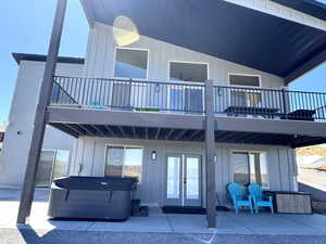 Back of house featuring a hot tub, board and batten siding, a patio, and a balcony