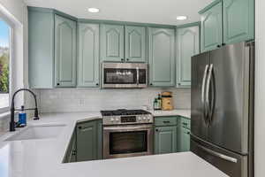 Kitchen with stainless steel appliances, a sink, green cabinets, tasteful backsplash, and light countertops