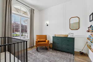 Bedroom with a nursery area, wood finished floors, a decorative wall, and baseboards