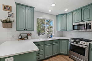 Kitchen with appliances with stainless steel finishes, green cabinetry, a sink, light wood-type flooring, and a textured ceiling