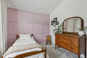 Bedroom with carpet floors, a decorative wall, and lofted ceiling