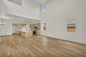 Unfurnished living room with baseboards, a high ceiling, a chandelier, and light wood-style flooring