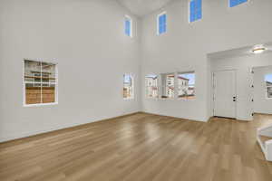 Unfurnished living room featuring a high ceiling, plenty of natural light, baseboards, and light wood-type flooring
