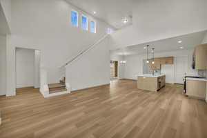Unfurnished living room featuring a high ceiling, a notable chandelier, a sink, and light wood-type flooring