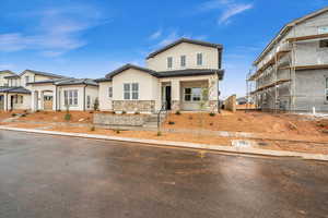 View of front of home featuring covered porch, stucco siding, a tile roof, and stone siding
