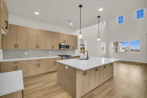 Kitchen with light brown cabinets, tasteful backsplash, a sink, light wood finished floors, and appliances with stainless steel finishes