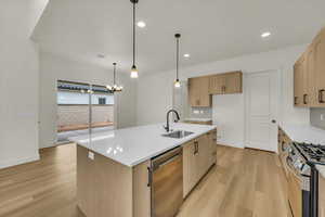 Kitchen featuring appliances with stainless steel finishes, decorative backsplash, a sink, and light wood-style flooring