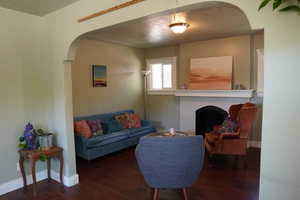 Living room featuring a fireplace, hardwood / wood-style floors, baseboards, a textured ceiling, and arched walkways