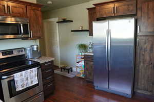Kitchen featuring light countertops, open shelves, appliances with stainless steel finishes, and dark wood-style floors