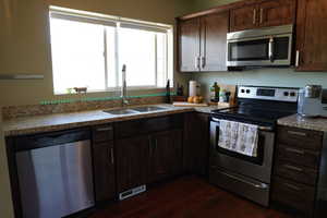 Kitchen featuring dark wood-style flooring, visible vents, appliances with stainless steel finishes, dark brown cabinets, and a sink