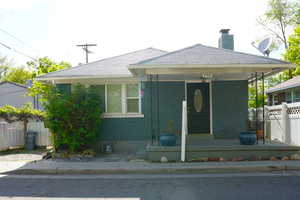 View of front facade featuring brick siding, fence, covered porch, and a chimney