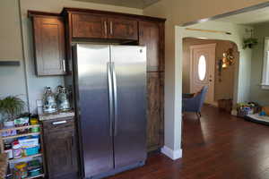 Kitchen featuring freestanding refrigerator, dark wood-style flooring, baseboards, light stone counters, and arched walkways