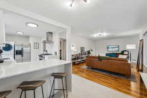 Kitchen featuring a peninsula, a breakfast bar, stainless steel appliances, wall chimney range hood, and washer / dryer