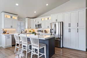 Kitchen featuring a sink, lofted ceiling, stainless steel appliances, decorative backsplash, and a kitchen island