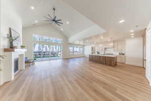 Unfurnished living room featuring high vaulted ceiling, a fireplace, a ceiling fan, recessed lighting, and light wood finished floors