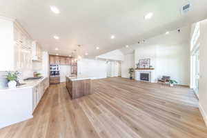Kitchen featuring light countertops, a fireplace, a kitchen island with sink, light wood finished floors, and recessed lighting