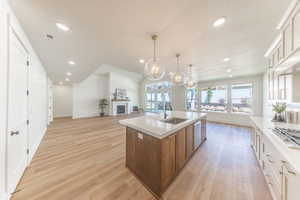 Kitchen with open floor plan, brown cabinets, a textured ceiling, light wood-style floors, and an island with sink