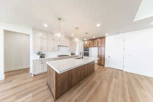 Kitchen featuring light wood finished floors, light countertops, a large island, recessed lighting, and decorative light fixtures
