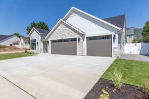 View of front of home featuring a garage, board and batten siding, concrete driveway, stone siding, and a gate