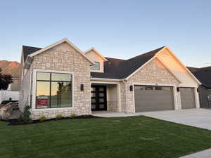 View of front of property with stone siding, an attached garage, a front lawn, driveway, and board and batten siding