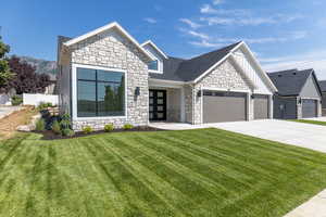 View of front of property featuring stone siding, board and batten siding, a front lawn, and a garage