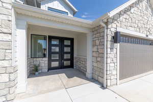 Property entrance featuring stone siding, french doors, a garage, and concrete driveway