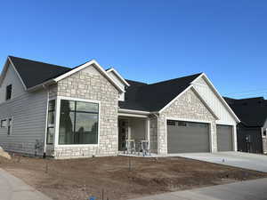 View of front of property featuring roof with shingles, stone siding, driveway, a garage, and board and batten siding