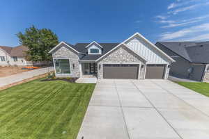 View of front of home featuring stone siding, board and batten siding, a front lawn, an attached garage, and concrete driveway