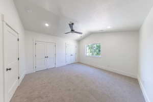 Unfurnished bedroom featuring light colored carpet, two closets, vaulted ceiling, recessed lighting, and a ceiling fan