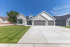 View of front of house with board and batten siding, stone siding, a front yard, a garage, and concrete driveway