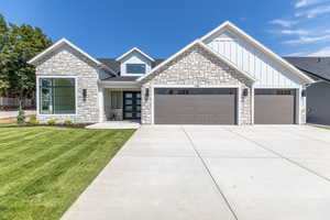 View of front of home with stone siding, a garage, a front yard, and board and batten siding