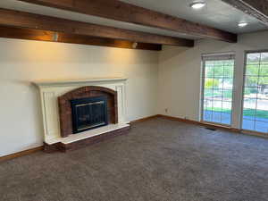 Unfurnished living room featuring a fireplace, carpet flooring, beamed ceiling, and visible vents