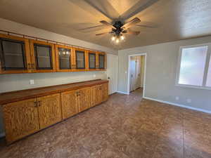 Kitchen featuring a ceiling fan, a textured ceiling, glass insert cabinets, brown cabinetry, and baseboards